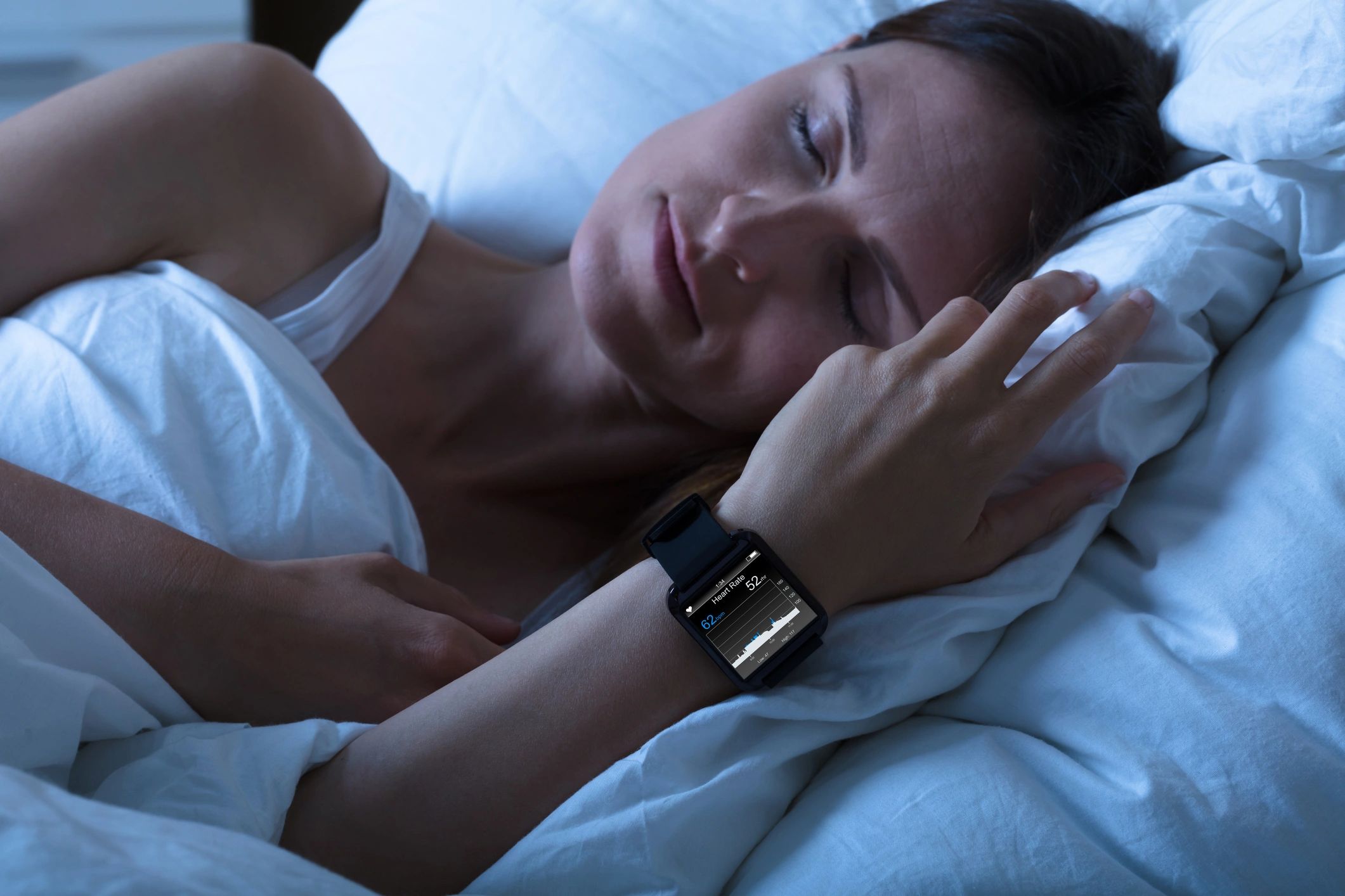 A woman sleeping in bed, wearing a smartwatch on her wrist.